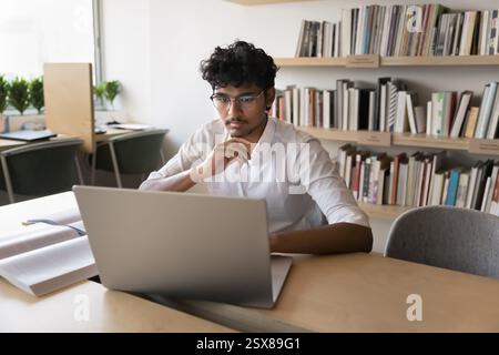 Konzentrierter Indianer, der auf Laptop in der Universitätsbibliothek studiert Stockfoto