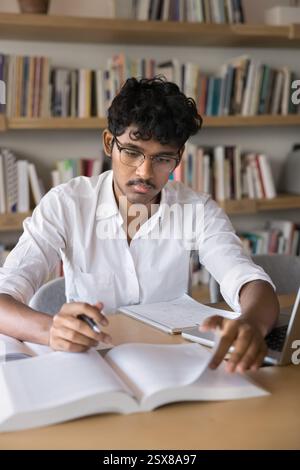 Indianer, der durch Lehrbuchseiten in der Bibliothek flippt Stockfoto