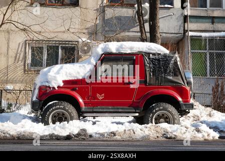 Bukarest, Rumänien – 22. Januar 2025: Seitenansicht des roten Autos Suzuki Samurai Pepper mit Schnee bedeckt vor dem Wohnblock. Alt off-ro Stockfoto