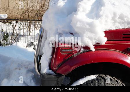 Bukarest, Rumänien – 22. Januar 2025: Samurai-Logo auf der Vorderseite des geparkten roten Autos Suzuki Samurai Pepper mit Schnee bedeckt Stockfoto