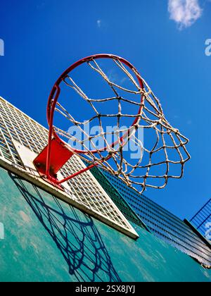Aufwärtstrend auf einen leeren, rot gestreiften Basketballkorb vor einem klaren blauen Himmel. Stockfoto