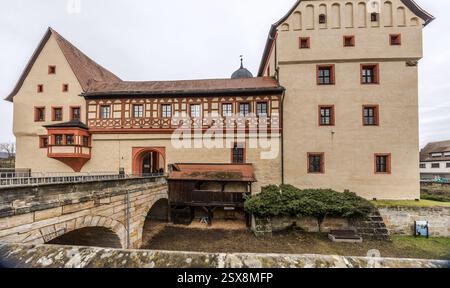 Ein asphaltierter Fußweg führt zur Kaiserpfalz in Forchheim und zeigt ein historisches Gebäude mit dekorativen Fachwerkelementen und gemeißelten Elementen. Ein Steinrelief und Säulen sind sichtbar. Forchheim, Bayern, Deutschland Eine Steinbrücke überspannt einen Innenhof vor einem historischen Schloss in Deutschland Menschen sind auf der Brücke zu sehen. Stockfoto