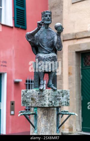 Die Bronzestatue des Konradsbrunnens zeigt König Konrad I. im Sitz, seine rechte Hand erhoben und eine Reichskugel in seiner Linken. Ein rosafarbenes Fachwerkhaus und grüne Fensterläden stehen im Hintergrund. Der Forchheimer Bildhauer Hans Dressel schuf den Brunnen 1998. Er erinnert an die Wahl des fränkischen Herzogs Konrad I. zum ostfränkischen König in Forchheim am 10. November 911 vor der St. Martins-Kollegiatkirche. Luitpoldstraße, Forchheim, Bayern, Deutschland. Stockfoto