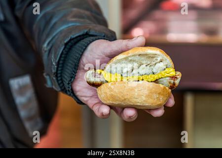 Eine Person in Deutschland hält ein Wurstsandwich mit Senf. Hauptstraße, Forchheim, Bayern, Deutschland Stockfoto