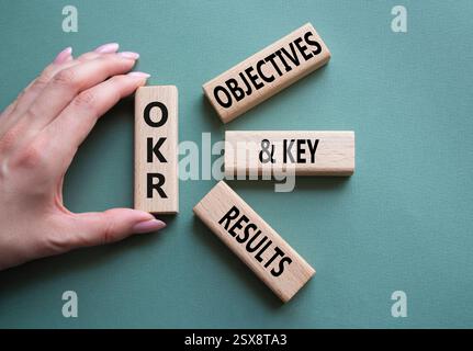 Symbol für OKR-Ziele und wichtige Ergebnisse. Holzblöcke mit den Worten OKR-Ziele und wichtige Ergebnisse. Geschäftsmann Hand. Wunderschöner graugrüner Hintergrund. Bus Stockfoto