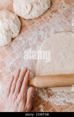 Verwenden Sie eine hölzerne Nudelnadel, um Teig auf einer bemehlten Oberfläche abzuflachen, um hausgemachte Pizza oder Brotbacken vorzubereiten Stockfoto
