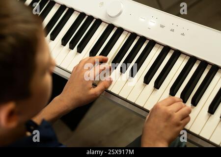 Draufsicht auf die Hände eines Jungen, die Klaviertasten auf einer digitalen Tastatur drücken. Zu Hause Klavier üben. Der Begriff der Bildung Stockfoto