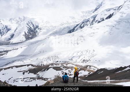 Mann und Frau genießen die Aussicht auf die Alpen- und Gletscherlandschaft vor ihnen, Pamir, Kirgisistan. Stockfoto