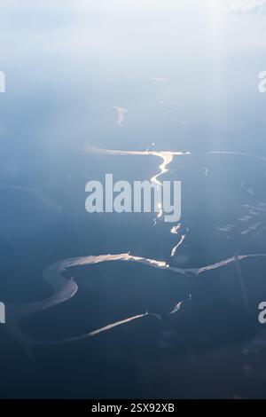 Ein ruhiger Blick aus der Luft, der die sich windenden Flüsse einfängt, während sie das Sonnenlicht in einer nebeligen Atmosphäre elegant reflektieren. Eine Silhouette eines Flusses, der sich windet Stockfoto