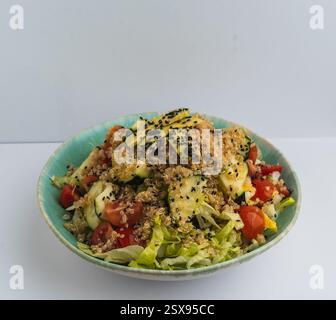 Farbenfroher Quinoa-Salat mit frischem Gemüse in einer türkisfarbenen Schüssel auf weißem Hintergrund Stockfoto
