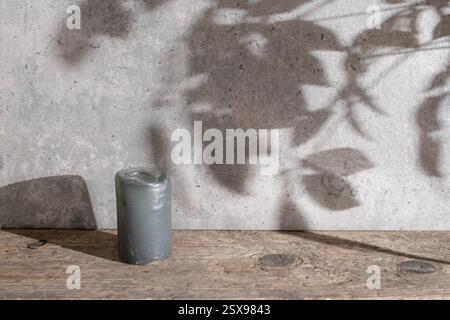 Wunderschöne Kulisse mit texturierten Wänden aus Zement, Schreibtisch aus verwittertem Holz und Schatten der Bäume, graue Kerze, Kopierraum Stockfoto
