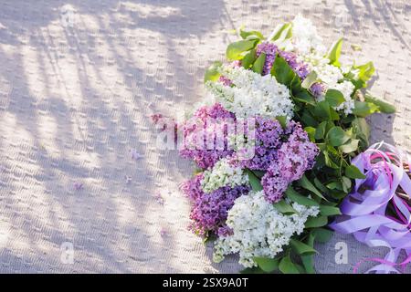 Schöne Fliederblüten im weichen Sonnenlicht auf einem gestrickten Stoffhintergrund, romantische Frühlingsblumenkomposition, Natur und saisonale Frische. Stockfoto