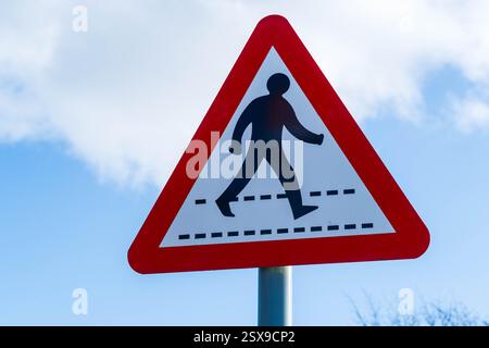 Ein britisches Verkehrsschild mit einem Fußgängerzebra, das vor Ihnen auf einem rot-weißen Warndreieck steht Stockfoto