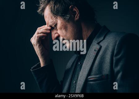 Gestresster und müder Geschäftsmann, der an Kopfschmerzen leidet, spät arbeitet und Überstunden hat, selektiver Fokus Stockfoto