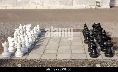 Schachset draußen, großes Brett und große Stücke Set. Weiße und schwarze Armee stehen auf gegenüberliegenden Seiten Stockfoto