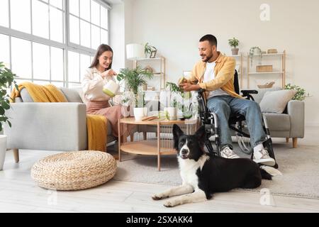 Junger Mann im Rollstuhl, mit Frau und Zimmerpflanzen zu Hause Stockfoto