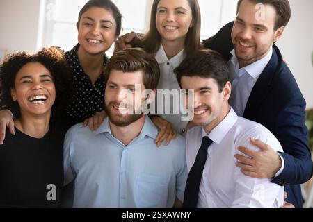 Gruppe junger attraktiver Arbeitskollegen, multiethnische Teammitglieder, die sich drinnen umarmen Stockfoto