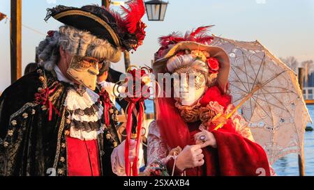 Venezianischer Karneval, kostümierte Paare in farbenfrohen historischen venezianischen Kostümen posieren bei Sonnenuntergang an der Lagune in Venedig, Italien Stockfoto