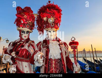 Venezianischer Karneval, kostümierte Paare in farbenfrohen historischen venezianischen Kostümen posieren bei Sonnenuntergang an der Lagune in Venedig, Italien Stockfoto