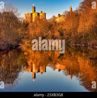 Ein Blick im frühen Frühling bei Sonnenuntergang auf Warkworth Castle in Northumberland spiegelt sich im Fluss Coquet mit einem schönen warmen Leuchten auf der Burg wider Stockfoto