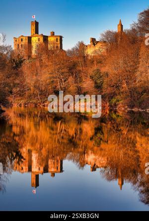 Ein Blick im frühen Frühling bei Sonnenuntergang auf Warkworth Castle in Northumberland spiegelt sich im Fluss Coquet mit einem schönen warmen Leuchten auf der Burg wider Stockfoto