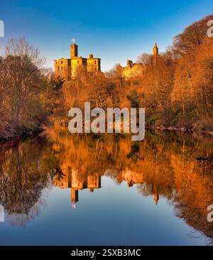 Ein Blick im frühen Frühling bei Sonnenuntergang auf Warkworth Castle in Northumberland spiegelt sich im Fluss Coquet mit einem schönen warmen Leuchten auf der Burg wider Stockfoto