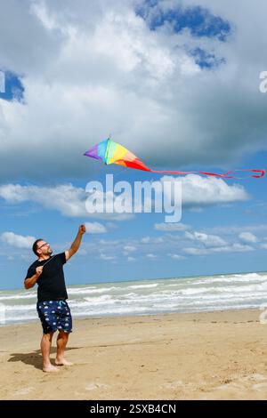 Weitwinkelansicht eines Mannes mittleren Alters, der an einem sonnigen Tag einen Drachen am Strand fliegt Stockfoto
