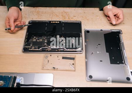Draufsicht des Computermeisters zur Reparatur der Laptop-Hauptplatine mit Schraubendreher, umgeben von verschiedenen Komponenten und Werkzeugen, Nahaufnahme. Computerkonzept Stockfoto