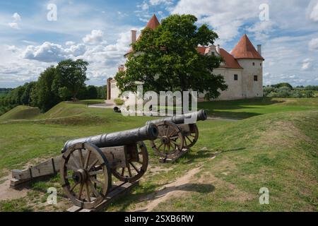 Zwei alte Retro-Kanonen. Lettische Touristenattraktion - mittelalterliche Burg Bauska auf Hintergrund. Bauska, Lettland. Stockfoto