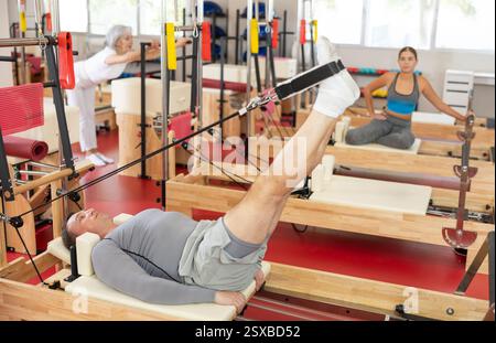 Der Mann ist in Pilates-Simulator mit Seilen und Seilen zum Dehnen der Beinmuskeln involviert Stockfoto