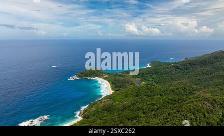 Türkisfarbenes Wasser kurvt sich um eine breite Bucht, die von grünen Hügeln und bewaldeten Gebieten unter einem teilweise bewölkten Himmel umgeben ist. Seychellen, Mahe. Stockfoto