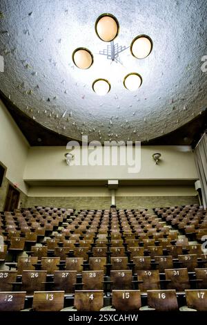 Großer Auditorium mit Stühlen von 1 bis 16. Die Stühle sind leer. Die Decke ist weiß und hat vier Lampen Stockfoto