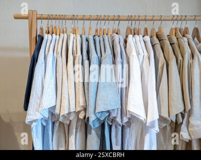 Kollektion von blauen, khakifarbenen und weißen Farben, minimalem Erdton von Relax Hemd in Kleiderbügeln, die an einer hölzernen Kleiderstange oder einem Kleiderständer auf weiß hängen Stockfoto