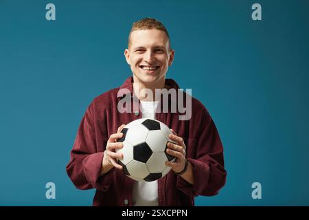 Lächelnder Junger Mann, Der Fußball Vor Blauem Hintergrund Hält Stockfoto