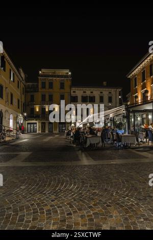 Abendessen auf einem platz, umgeben von beleuchteten historischen Gebäuden, Nachtfotos mit langer Belichtungszeit, aufgenommen in Peschiera del Garda, Italien V Stockfoto