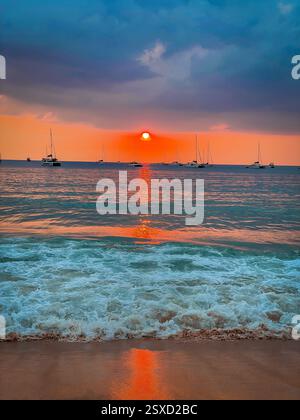 Leuchtender Sonnenstrahl auf dem ruhigen Meer, Boote und Wellen bei Sonnenuntergang die leuchtend orange Sonne geht langsam am Horizont unter und wirft einen magischen Lichtstrahl, der tanzen lässt Stockfoto