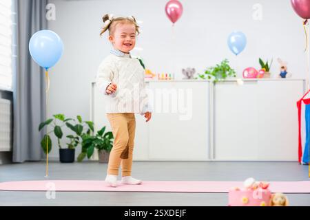 Niedliches 4-jähriges Mädchen mit Down-Syndrom feiert ihren Geburtstag in einem mit Ballons dekorierten Spielzimmer. Kindergeburtstag. Stockfoto