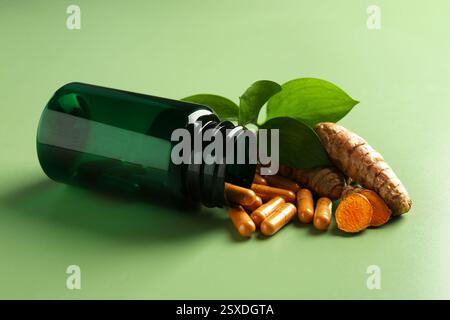 Kurkuma Kapseln, Wurzeln und umgedrehte medizinische Flasche auf grünem Hintergrund Stockfoto