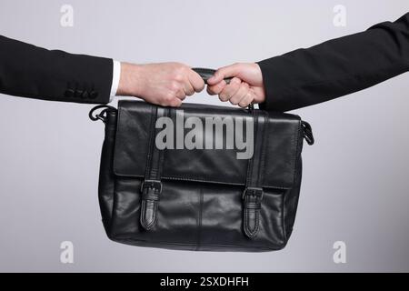 Wettbewerbskonzept. Geschäftsleute ziehen Lederaktentasche auf grauem Hintergrund, Großaufnahme Stockfoto