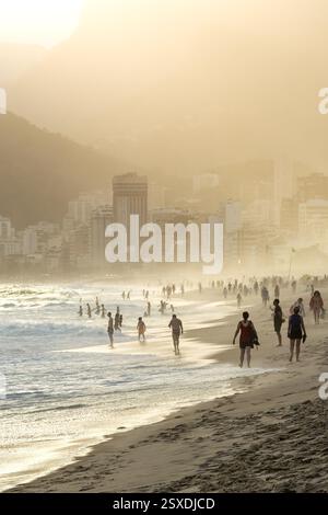 Vertikale Aufnahme von Menschen, die während des Sonnenuntergangs am Strand von Ipanema in Rio de Janeiro spazieren Stockfoto