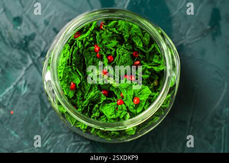 Getrocknete Basilikumblätter und rosa Pfeffer in einem Glasgefäß auf Malachithintergrund. Nahaufnahme. Blick von oben. Hochwertige Fotos Stockfoto