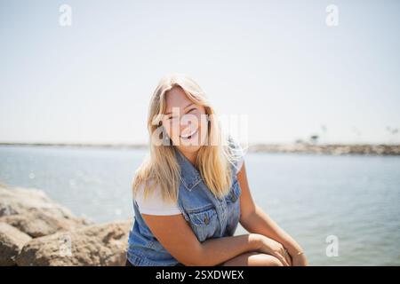Eine junge Frau, die auf einem Felsen am Meer sitzt Stockfoto