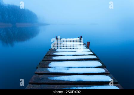Schnee auf dem Steg und ein ruhiger nebeliger See Stockfoto
