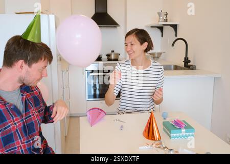 Das junge Paar feiert zu Hause gemütlich Geburtstag und genießt Kuchen und Lachen in warmer Atmosphäre. Fröhliche Atmosphäre, farbenfrohe Dekoration, Vorbereitung auf holi Stockfoto