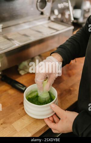Barista rührt im Coffee Shop leuchtend grünen Matcha in einer Keramikschale Stockfoto