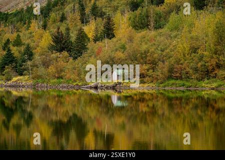 Kleine Hütte, die sich in einem See spiegelt, umgeben von bunten Herbstbäumen Stockfoto