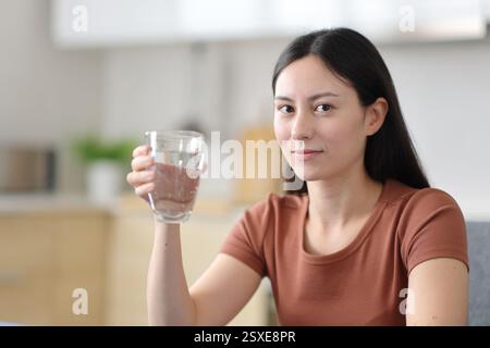 Ernsthafte asiatische Frau, die ein Glas Wasser in der Küche zu Hause hält Stockfoto