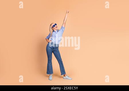 Stilvolle junge Frau auf beigefarbenem Hintergrund mit trendiger Jeanshose und gestreiftem Hemd Stockfoto