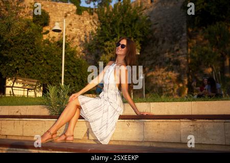 Lächelnde Frau, die sich bei Sonnenuntergang auf der Bank entspannt Stockfoto