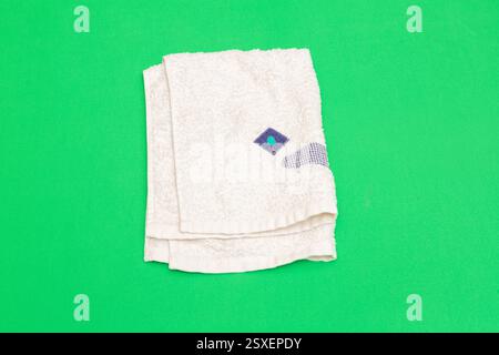 Gefaltetes weißes Handtuch mit kleiner blauer und grüner Stickerei auf leuchtendem grünem Hintergrund für eine einfache, aber optisch ansprechende Szene Stockfoto